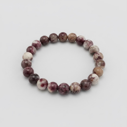 A beaded stretch bracelet made of round stone beads in shades of burgundy, purple, brown, and cream, resting on a wooden table outdoors.
